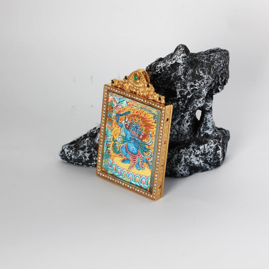 Angled view of Acalanatha (Fudo Myo-o) mini thangka pendant showing the thickness and structure of the double-sided titanium steel case, ornate top crest with green stone detail, and vivid hand-painted artwork