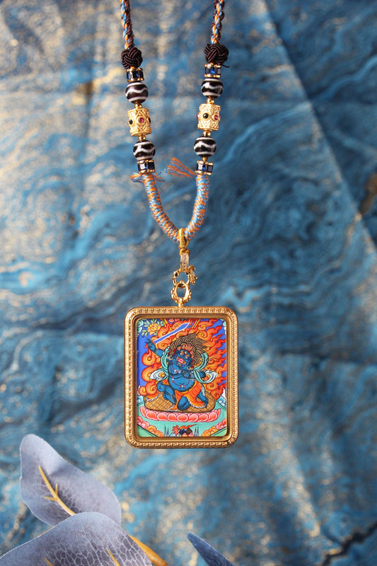 Close-up photo of the Acalanatha (Fudo Myo-o) hand-painted mini thangka inside a gold-tone titanium steel case, highlighting the vivid flames, figure details, and bead-and-knot cordwork.