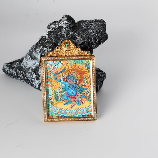 Front view of Acalanatha (Fudo Myo-o) mini thangka pendant, fierce blue Wisdom King with raised sword and flame halo, hand-painted with mineral pigments, set in a gold-tone double-sided jewelry-grade titanium steel case with crystal-style border