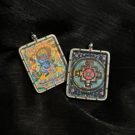 Front and back view of an Acalanatha (Fudo Myo-o) mini thangka pendant showing the fierce blue deity standing on a lotus with flames behind him and a sacred mandala design on the reverse, enclosed in a square 925 sterling silver pendant case with gemstone accents.