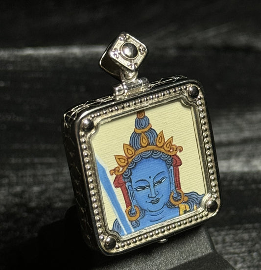 Angled view of a miniature Akashagarbha Bodhisattva thangka pendant highlighting the blue hand-painted deity portrait and textured silver pendant frame.