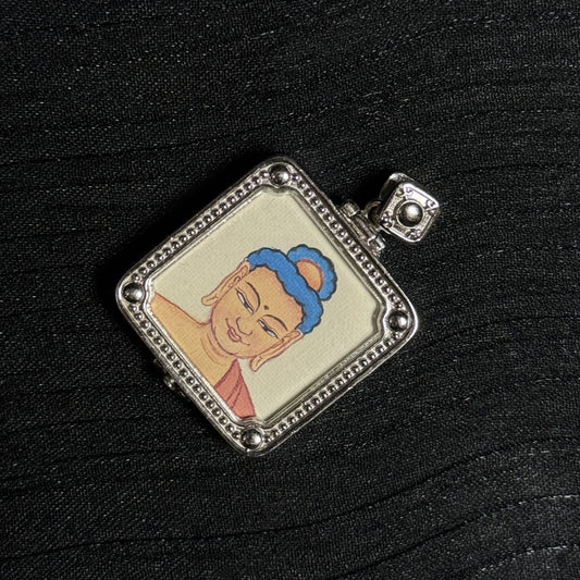 Angled view of a Tibetan Amitabha Buddha miniature thangka pendant showing the hand-painted Buddha portrait and textured silver frame.