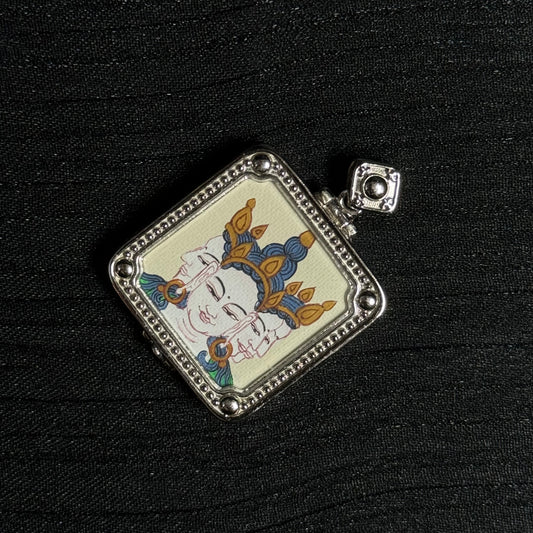 Angled view of a miniature Vairocana Buddha thangka pendant highlighting the hand-painted three-faced Buddha image and textured silver pendant frame.