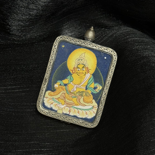 Angled view of Yellow Jambhala thangka pendant highlighting coarse mineral pigment texture, golden deity body color, and engraved silver frame details