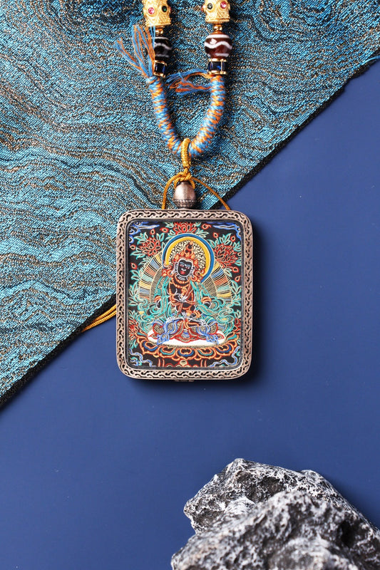 Close-up of Vajrasattva mini thangka pendant with black-gold painting, fine mineral pigment lines, and carved silver frame.