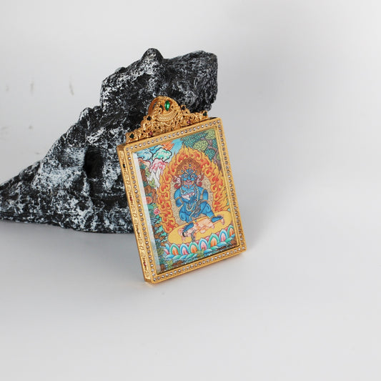 Angled view of Black Jambhala mini thangka pendant showing the thickness and structure of the titanium steel case, with ornate top crest and detailed hand-painted thangka artwork visible inside