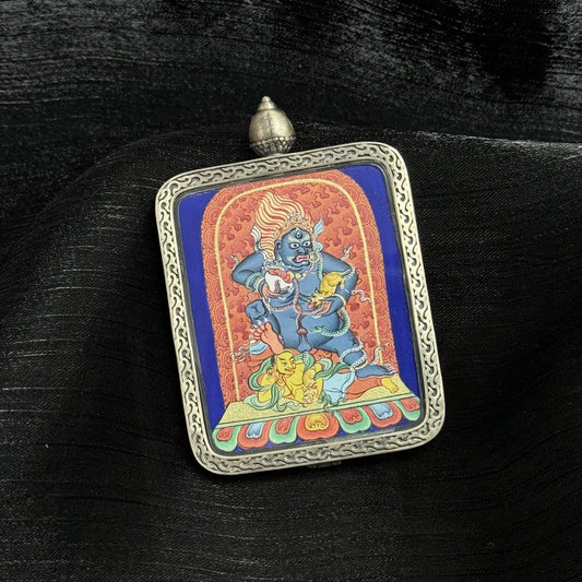 Left angled view of Black Jambhala Tibetan mini thangka pendant showing detailed hand-painted wealth deity inside silver protective frame.