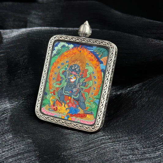 Angled view of Black Jambhala thangka pendant displaying detailed mineral pigment painting, vibrant deity iconography and traditional Tibetan silver pendant frame