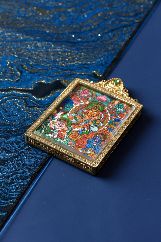 Angled flat lay of Five Wealth Deities mini thangka pendant showing the jeweled titanium steel frame and hand-painted thangka artwork, Nepal series