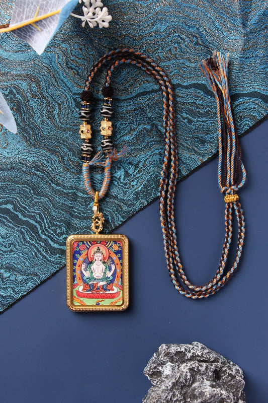 Four-Armed Avalokiteshvara (Chenrezig) mini thangka pendant showing the hand-painted deity image with mineral pigment colors, rectangular titanium steel case, raised border detailing, and bead-and-braided cord attachment at the top.