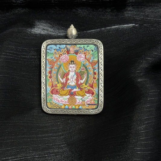 Angled view of Four-Armed Avalokiteshvara mini thangka pendant, hand-painted with mineral pigments, seated on lotus throne with four arms and halo, set in Dunhuang Nine-Colored Deer engraved silver gawu case.