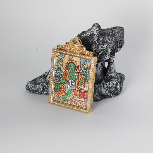 Angled view of the Green Tara mini thangka pendant highlighting the crystal-set border around the frame, the gold-tone case depth, and the ornate crown top with green and multicolor stones.