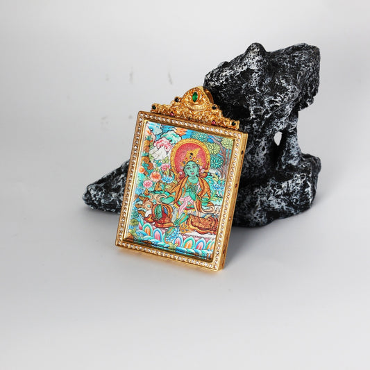 Angled view of Green Tara mini thangka pendant showing thickness and craftsmanship of the jewelry-style titanium steel frame, hand-painted mineral pigment artwork visible beneath protective casing