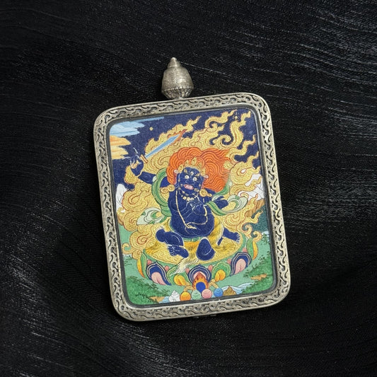 Close angled view of Acalanatha mini thangka pendant showing detailed hand-painted mineral pigment thangka artwork inside a silver pendant frame