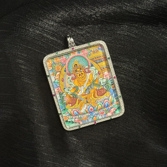 Close-up of a hand-painted Yellow Jambhala mini thangka pendant depicting the Tibetan wealth deity seated on a lotus throne surrounded by floral motifs and traditional temple architecture.