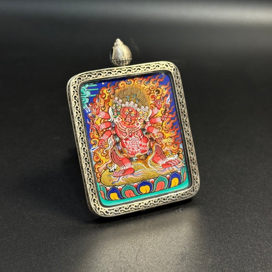Angled view of Hayagriva mini thangka pendant highlighting the fierce deity expression, multiple arms, flame halo and vibrant mineral pigment colors inside a decorative sterling silver frame.