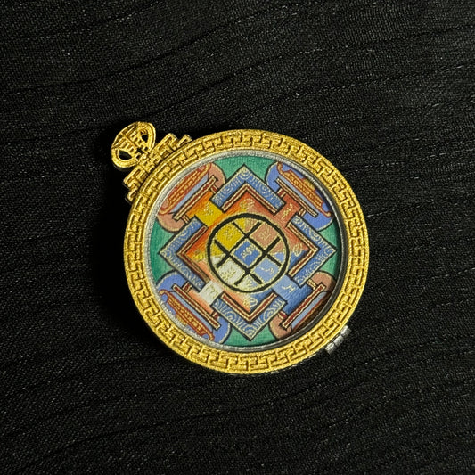 Angled view of a Yamantaka Mandala miniature thangka pendant showing detailed hand-painted mandala geometry and gold decorative frame.