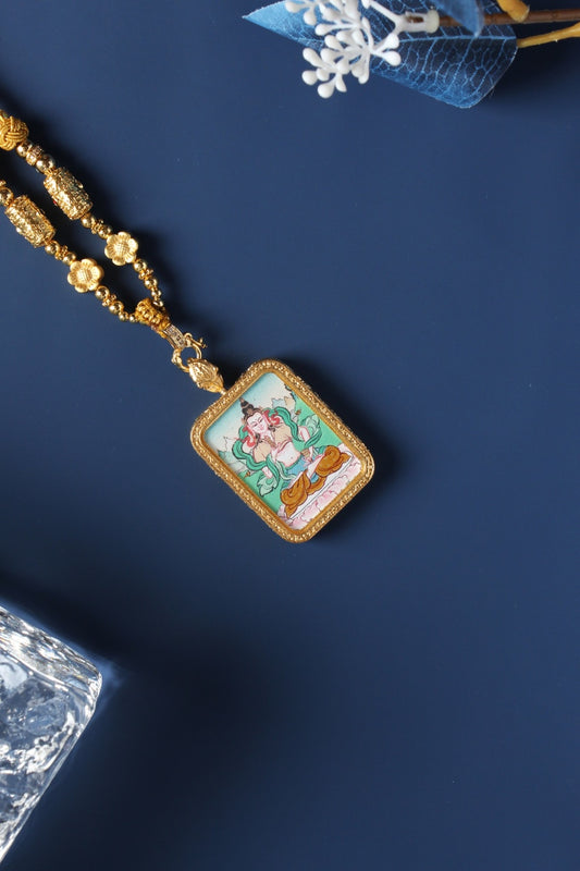Close-up of Vajrasattva mini thangka pendant showing fine line work, mineral pigment layers, gold-tone frame, and hanging connector details