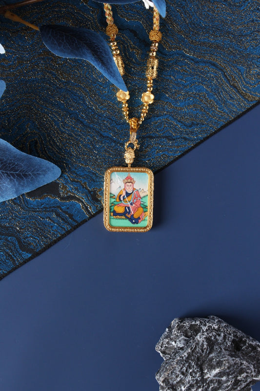 Hand-painted Ksitigarbha (Dizang) mini thangka pendant displayed with gold-tone beaded necklace, rectangular double-sided titanium steel case, mineral pigment artwork visible