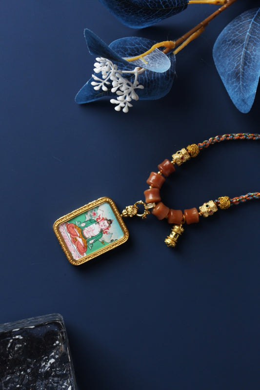 Mahasthamaprapta Bodhisattva mini thangka pendant necklace showing a hand-painted Bodhisattva seated on a lotus base inside a rectangular metal frame, with braided cord and orange bead details