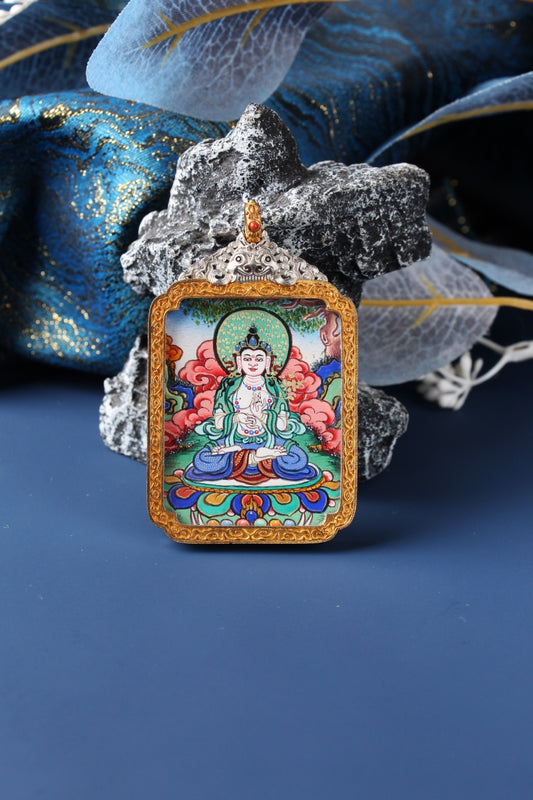Front view of Mahasthamaprapta Bodhisattva mini thangka pendant, fully hand-painted with mineral pigments, set in an ornate silver-plated case with gold-tone frame, photographed against blue brocade fabric with stone and translucent leaf decor.