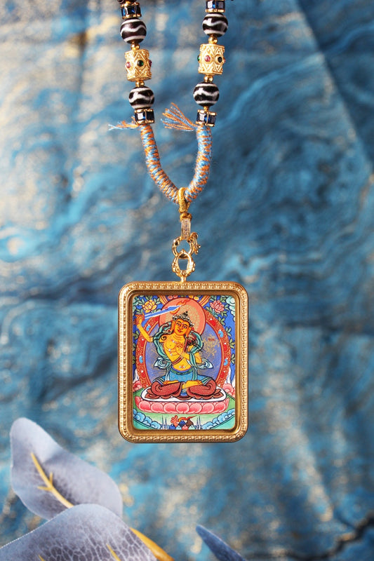 Close-up of the Manjushri Bodhisattva mini thangka pendant showing fine linework, detailed iconography, saturated mineral pigment layers, ornate frame border, and the bead-and-braided cord section near the pendant loop.