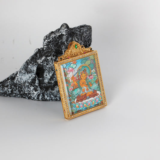 Close angled view of a hand-painted Manjushri Bodhisattva thangka pendant, featuring vivid turquoise and gold tones inside a crystal-studded frame.