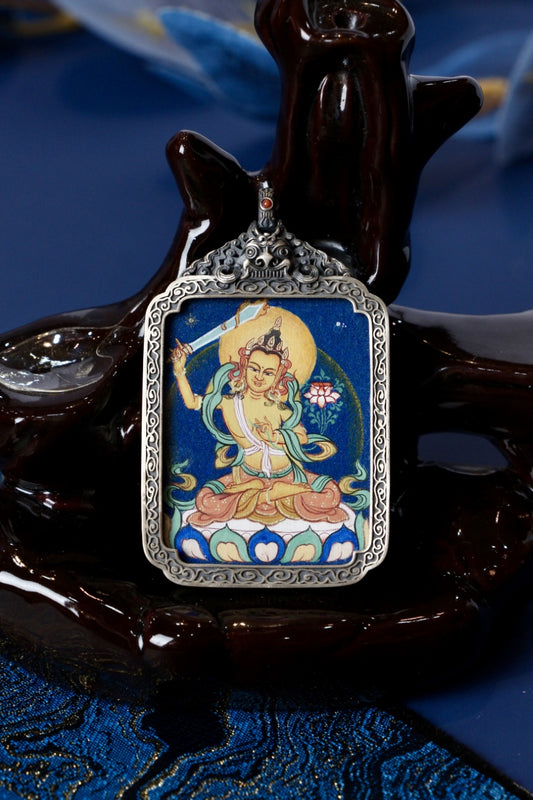 Front view of a Manjushri Bodhisattva mini thangka pendant, hand-painted with mineral pigments and set in a vintage-style silver case.
