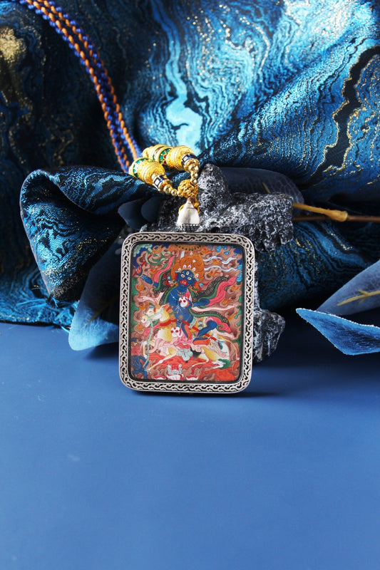 Front close-up of a Palden Lhamo mini thangka pendant depicting the wrathful protector riding a mule, with vivid mineral pigment colors and fine linework, framed in a silver case with decorative bead cord