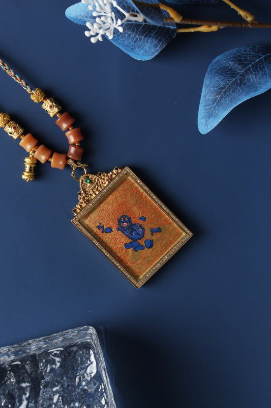 Angled view of Acalanatha mini thangka pendant showing gold thangka linework, layered mineral pigments, gemstone-accented titanium steel frame, and traditional braided cord connection