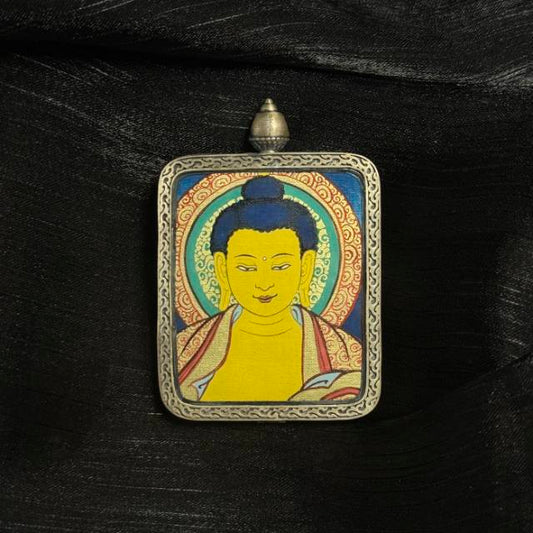 Angled view of Shakyamuni Buddha mini thangka pendant showing hand-painted Buddha portrait with mineral pigments inside a traditional silver pendant frame