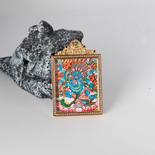 Angled view of the Six-Armed Mahakala mini thangka pendant showing the thickness of the gold-tone titanium steel case, crystal border, and enclosed double-sided structure.