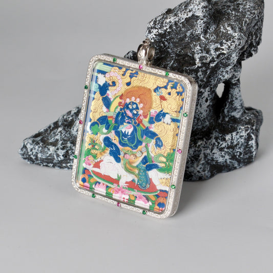 Front angled view of a hand-painted Six-Armed Mahakala mini thangka pendant in a jewelry-grade silver case with a gemstone-set border, showing coarse mineral pigment layering and detailed cloud patterns, painting size 4 × 5 cm.