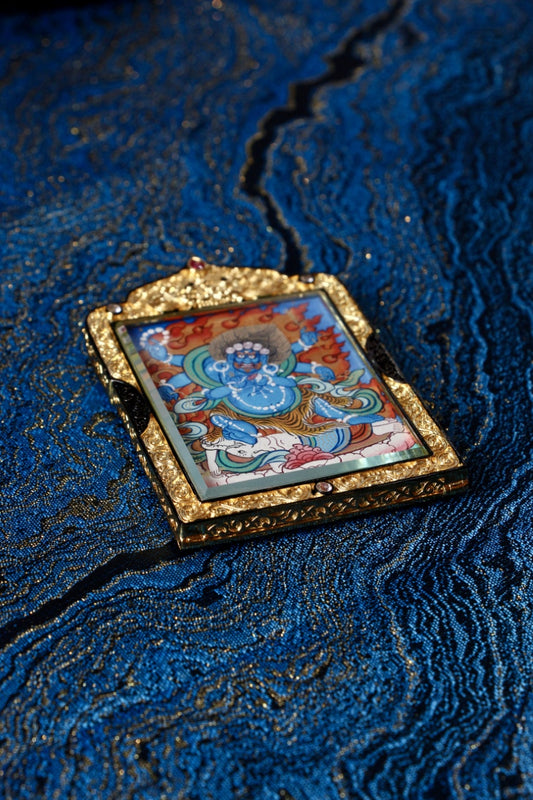 Angled view of Six-Armed Mahakala Thangka pendant showing detailed hand-painted blue cloud background and mineral pigment artwork from Rebgong tradition