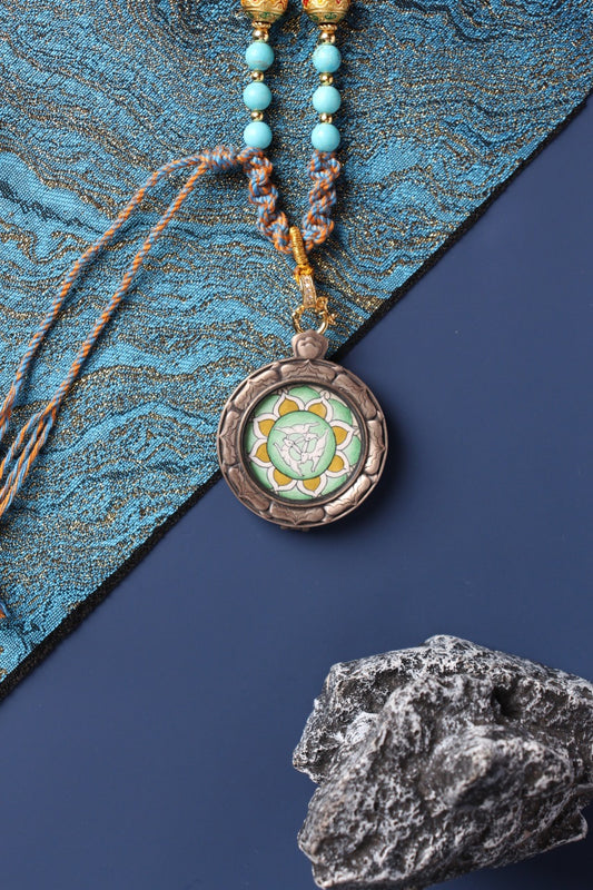 Close-up view of the Three Hares (shared-ear triskelion) hand-painted mini thangka artwork in green tones, set inside a round 925 silver pendant case with engraved details and braided cord.