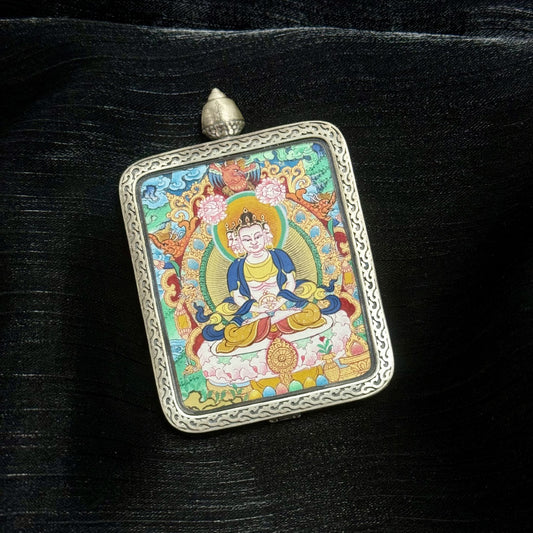 Angled view of Vairocana Buddha miniature Tibetan thangka pendant in engraved silver case, detailed Menri style painting with vivid mineral colors.