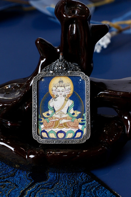 Front view of a Vairocana (Mahavairocana) mini thangka pendant in an antique silver case, painted with Tibetan mineral pigments, displayed on a dark stand.