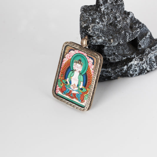 Angled view of Vairocana mini Thangka pendant highlighting the layered mineral pigment colors, fine crown and facial details, and the ornate engraved silver border around the rectangular pendant.