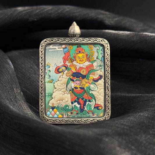 Angled view of Vaishravana Northern Guardian King mini thangka pendant showing Tibetan hand-painted deity artwork inside a silver pendant frame