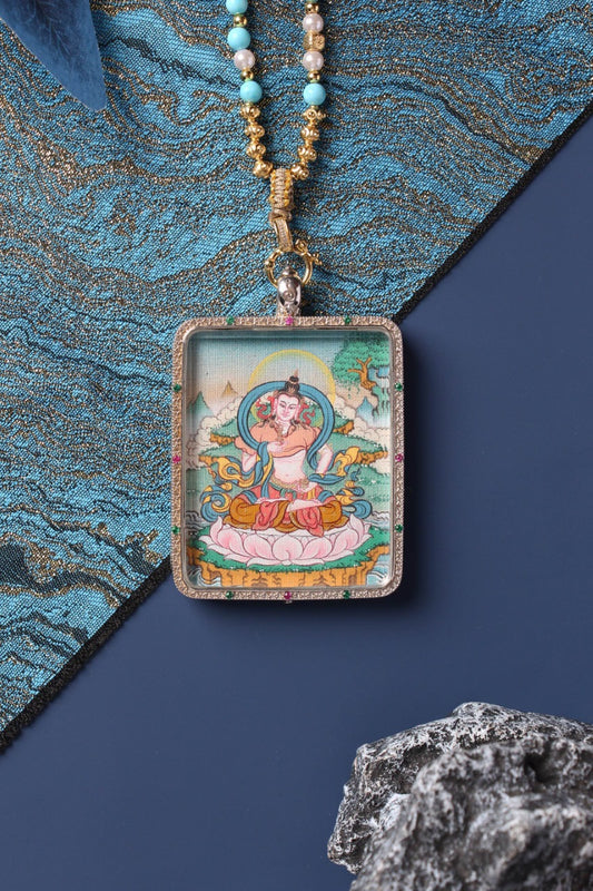 Front close-up of a Vajrasattva mini thangka pendant, hand-painted with mineral pigments, showing Vajrasattva seated on a lotus with flowing scarves and halo, set in a rectangular 925 sterling silver jewelry case with small colored stone accents and beaded necklace.