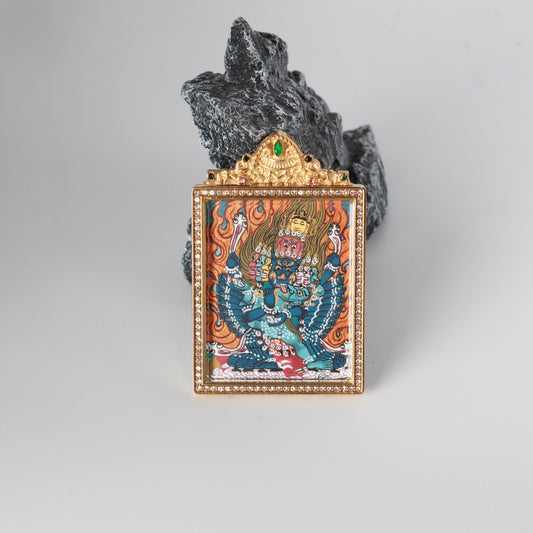 Front view of a hand-painted Yamantaka mini thangka pendant in a gold-tone titanium steel jewelry case with a crystal-set frame and green gemstone top accent, 4 × 5 cm.