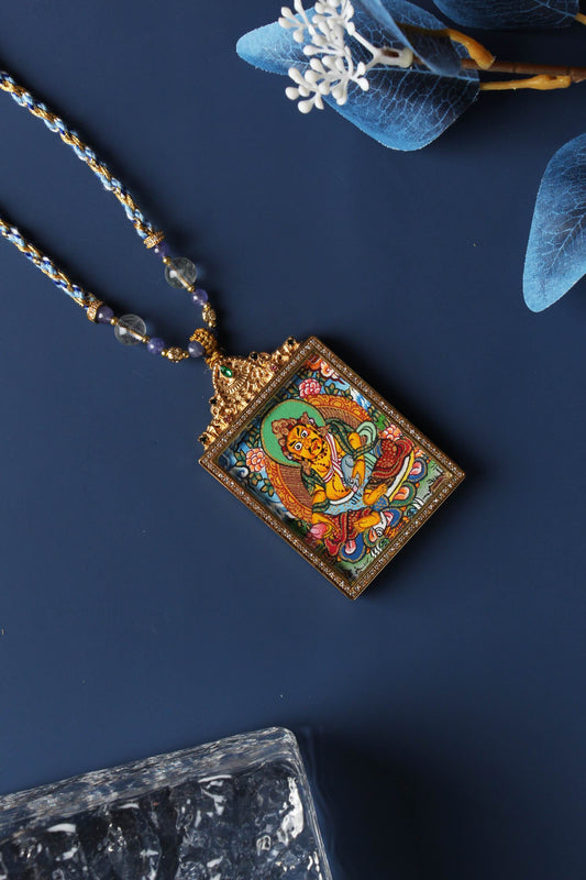 Square Yellow Jambhala thangka pendant shown at an angle, featuring colorful Tibetan Buddhist artwork and decorative necklace details