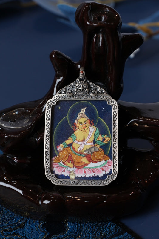 Close-up of Yellow Jambhala (Dzambhala) hand-painted mini thangka set inside an ornate vintage-silver gawu pendant case