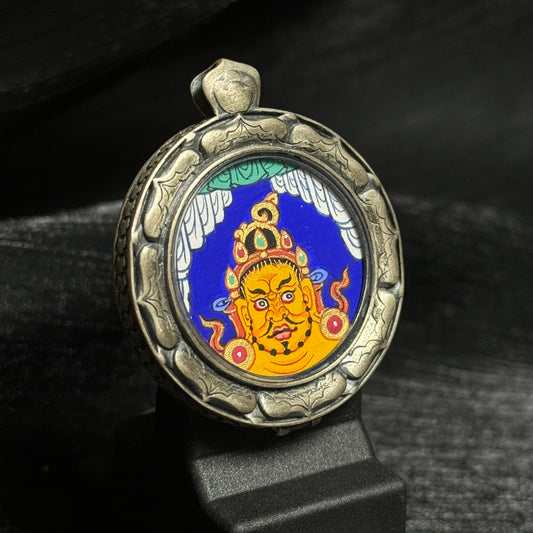 Angled view of the Yellow Jambhala head mini thangka pendant showing the detailed deity portrait painting and the textured 925 silver pendant case.