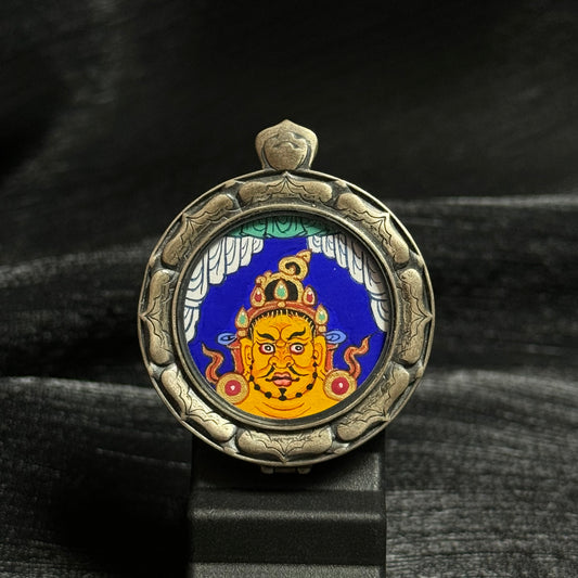 Front view of a Yellow Jambhala head mini thangka pendant hand-painted with mineral pigments in Rebgong style, set inside a carved 925 silver protective frame.
