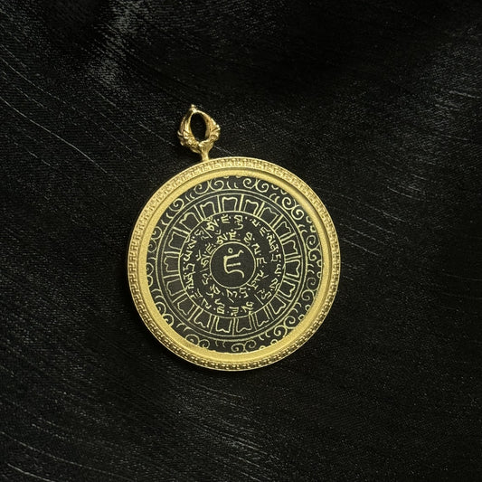 Close-up of a Yellow Jambhala heart mantra mini thangka pendant showing hand-written gold powder Tibetan script on a black background with a gold-tone circular rim.