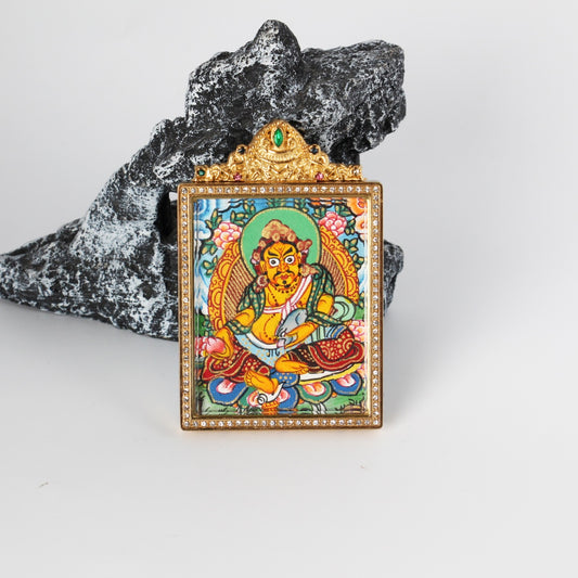 Angled view of Yellow Jambhala mini thangka pendant, hand-painted with mineral pigments, set in a gold-tone titanium steel case with crystal-style border and ornate top detail