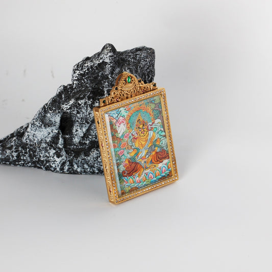 Angled view of Yellow Jambhala mini thangka pendant showing the thickness and structure of the titanium steel case, with finely detailed hand-painted Nepalese thangka artwork visible inside