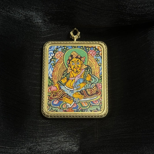 Hand-painted Yellow Jambhala mini thangka pendant from Nepal showing the Buddhist wealth deity seated on a lotus throne, surrounded by floral motifs and traditional Himalayan patterns within a titanium steel pendant frame.