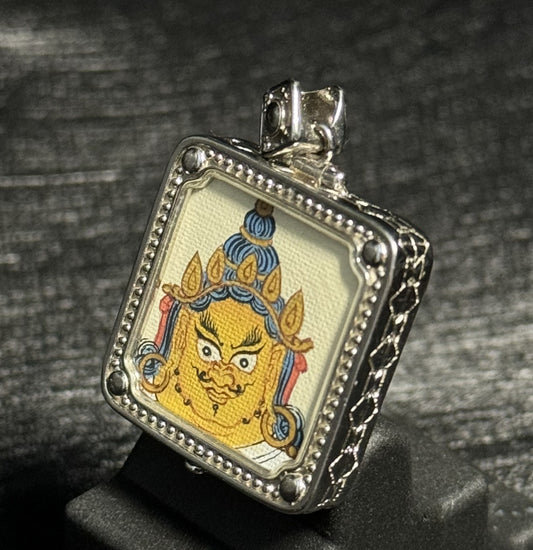 Angled view of Yellow Jambhala mini thangka pendant showing detailed Tibetan wealth deity painting with mineral pigment colors